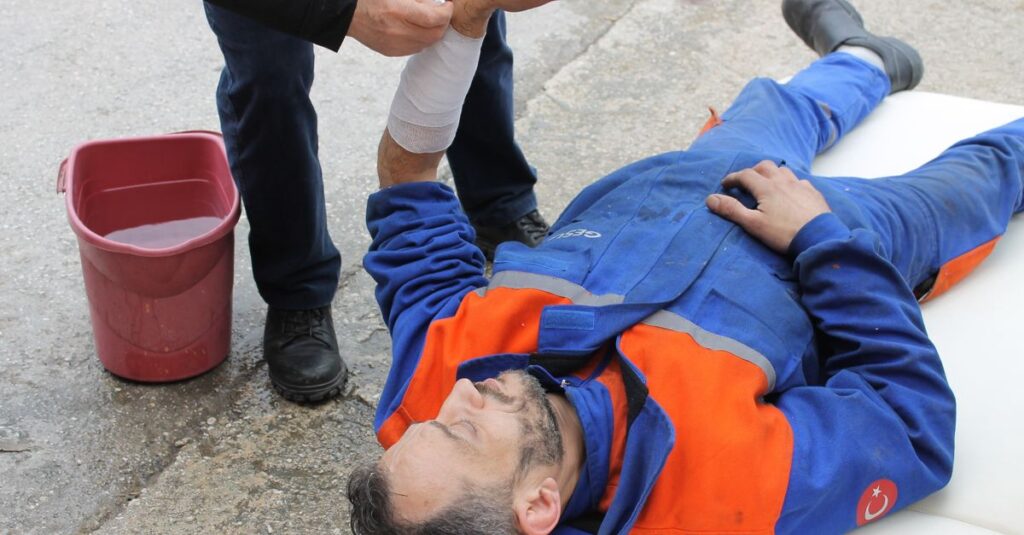 Injured worker receiving first aid on-site with arm bandage applied.